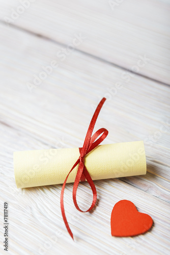 Rolled paper and red heart on vintage wooden background