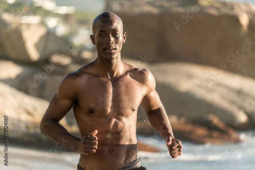 Topless, muscular black man running on beach