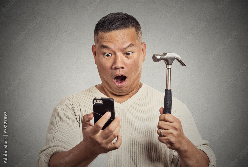 Shocked man looking at smart phone holding hammer Shocked man looking at smart phone holding hammer