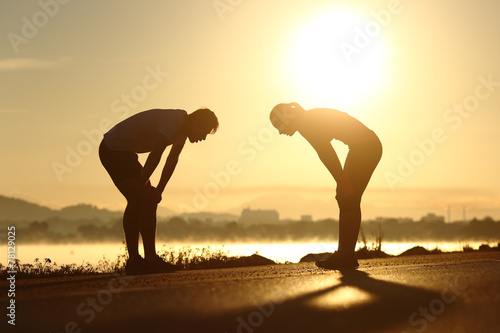 Exhausted and tired fitness couple silhouettes at sunset