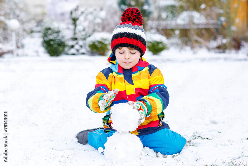 Funny preschool boy in colorful clothes making a snowman Funny preschool boy in colorful clothes making a snowman