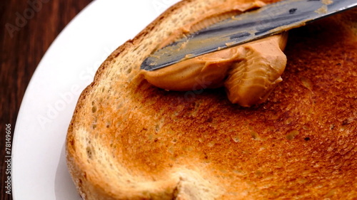 Tasty creamy peanut butter being spread on white toast