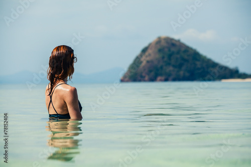 Woman sitting in water looking at island © LoloStock