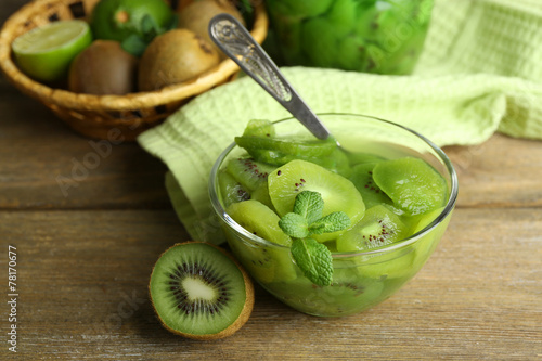 Tasty kiwi jam in glass bowl and jar on wooden background