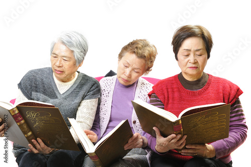分厚い本を読んで勉強している高齢者のおばあさん3人組