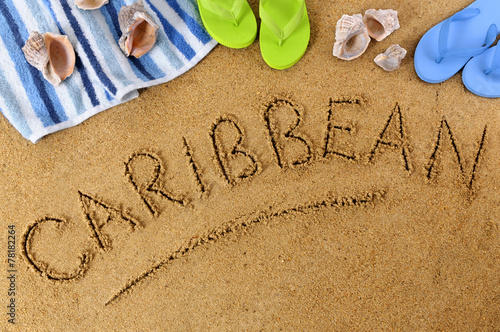 The word Caribbean written in sand on a beach with towel flip flops seashells summer vacation holiday photo