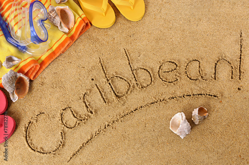 The word Caribbean written in sand on a beach with towel flip flops seashells summer vacation holiday photo
