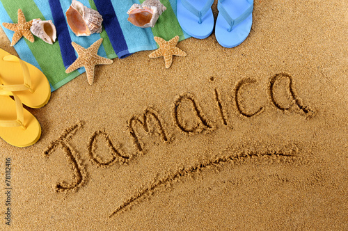 The word Jamaica written in sand on a beach with towel flip flops seashells Caribbean summer vacation holiday photo