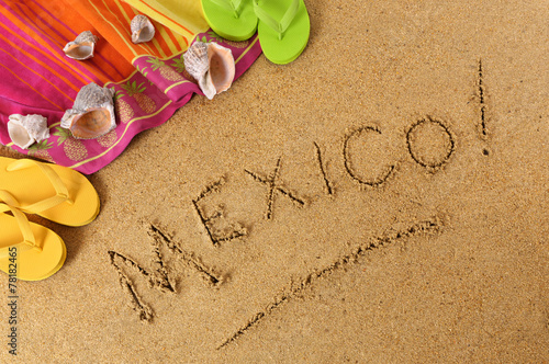 The word Mexico written in sand on a beach with towel flip flops seashells Mexican summer vacation holiday photo