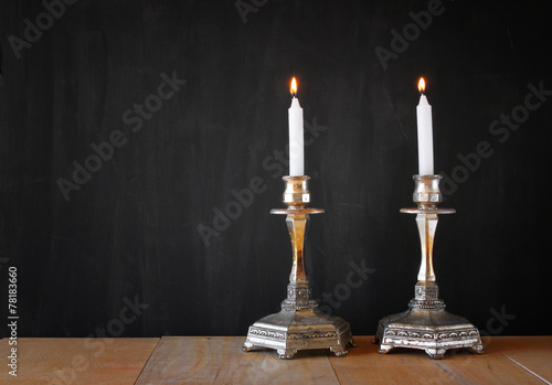 two candlesticks with burning candels over wooden table and blac