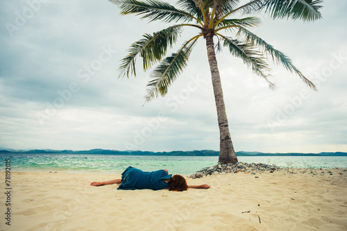 Young woman lying under palm tree on beach