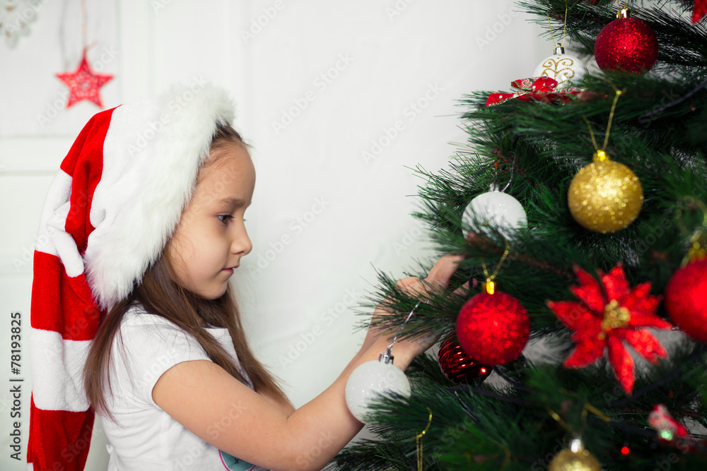 little girl in  red cap hangs on the Christmas tree new year