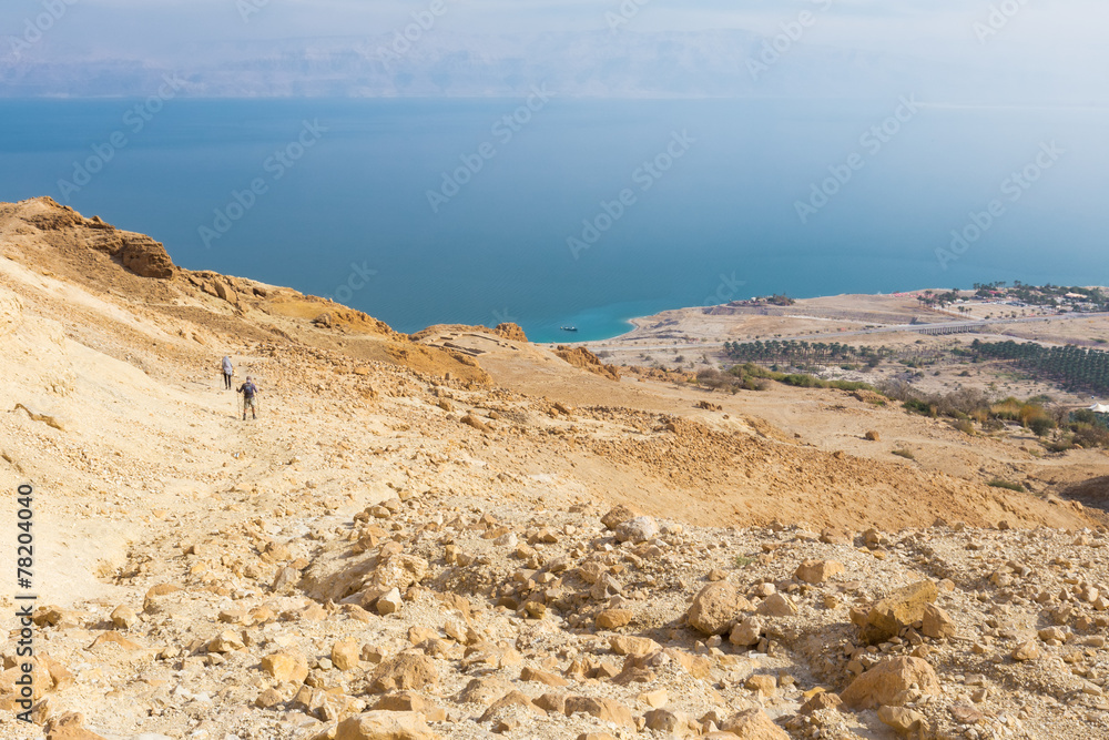 Couple walking desert trail down to Dead sea.