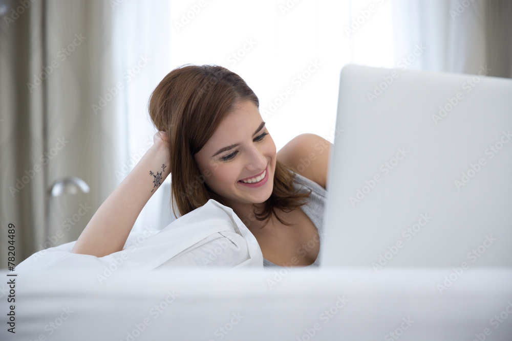 Portrait of a smiling woman lying on the bed with laptop at home Portrait of a smiling woman lying on the bed with laptop at home