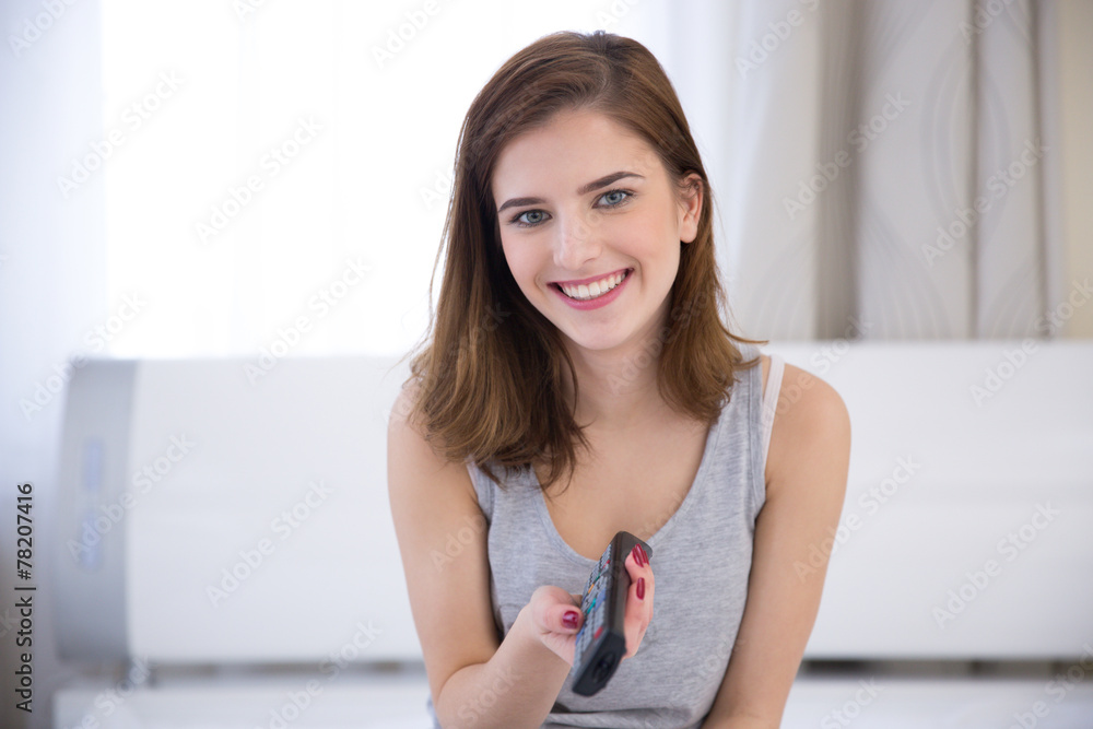 Smiling woman sitting on the bed with remote control Smiling woman sitting on the bed with remote control