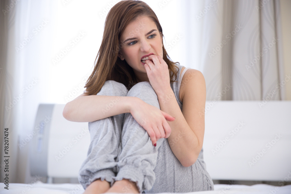 Worried young woman sitting on the bed at home Worried young woman sitting on the bed at home
