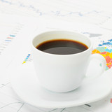 Cup of coffee over world map and financial documents next to it