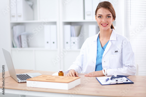 Beautiful young smiling female doctor sitting at the desk and