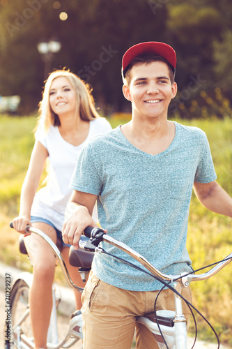 Young man and woman riding a bicycle in the park outdoors