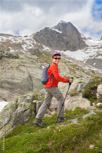 Kid with backpack and sticks ascents on mountain slope