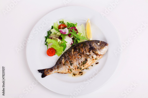 baked whole fish grilled on a plate with vegetables and lemon