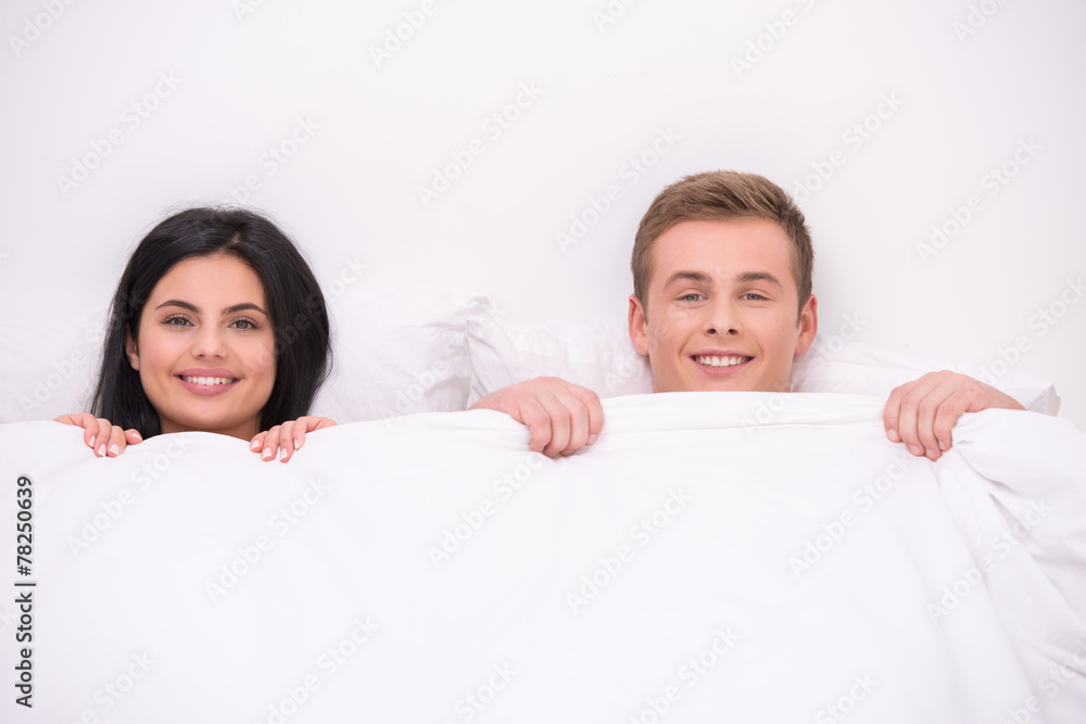 Happy couple is under blanket looking at camera Happy couple is under blanket looking at camera