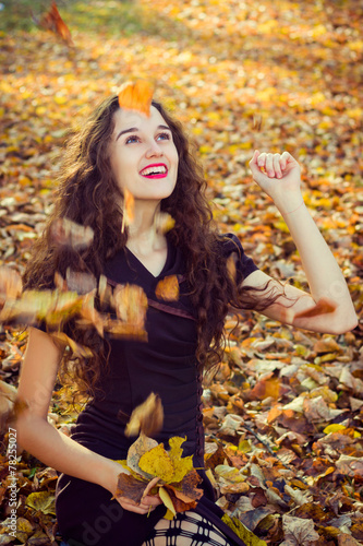Happy girl playing leaves in the autumn park