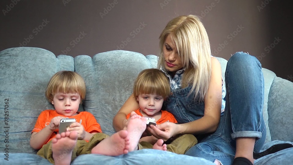 Mother and little sons twins on couch playing with mobile phones Mother and little sons twins on couch playing with mobile phones