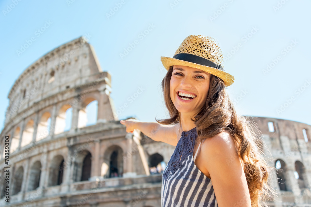 Smiling young woman pointing on colosseum in rome, italy