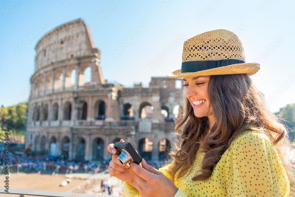 Fototapeta premium Happy woman checking photos in camera in front of colosseum