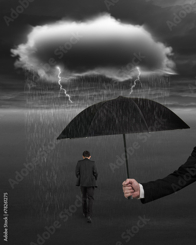 Hand holding umbrella protecting businessman from dark cloud rai
