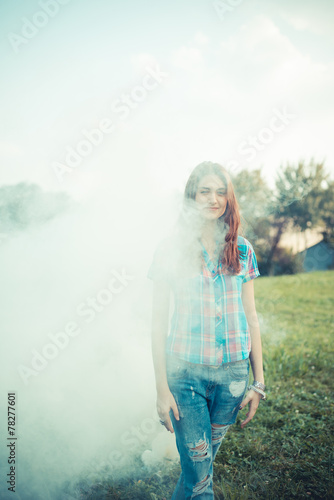 Fototapeta Naklejka Na Ścianę i Meble -  Portrait of smiling young woman standing in smoke outdoors