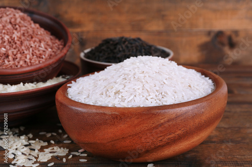 Different kinds of rice in bowls on wooden background
