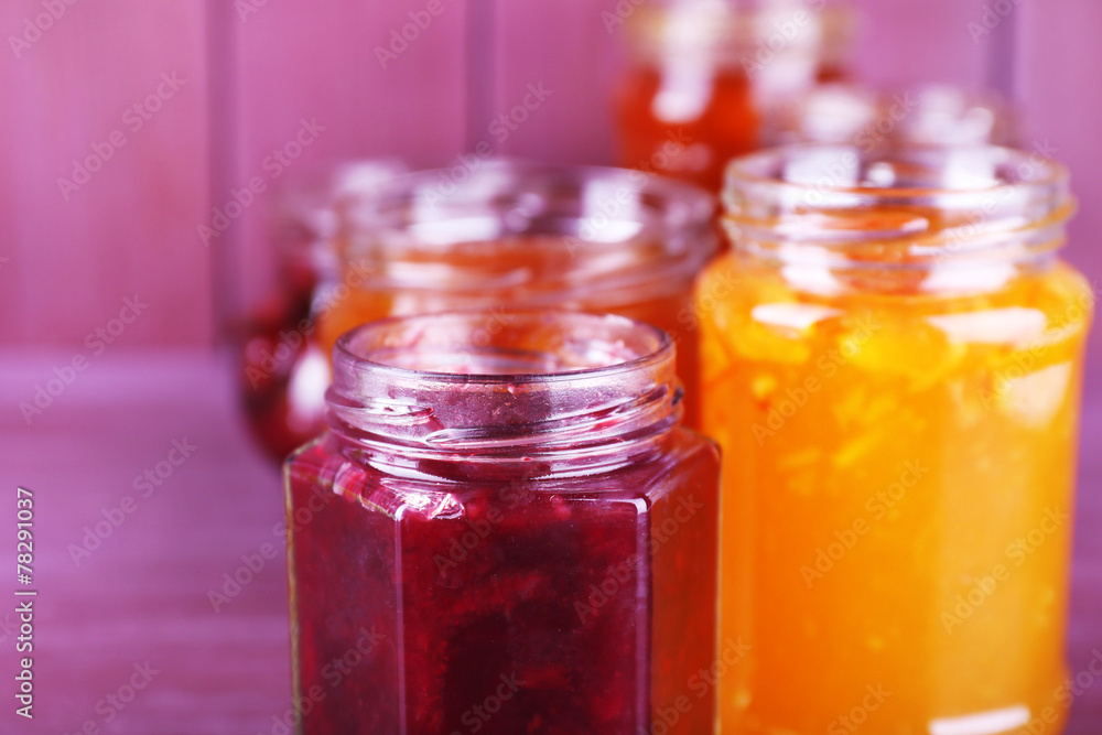 Homemade jars of fruits jam on color wooden background Homemade jars of fruits jam on color wooden background