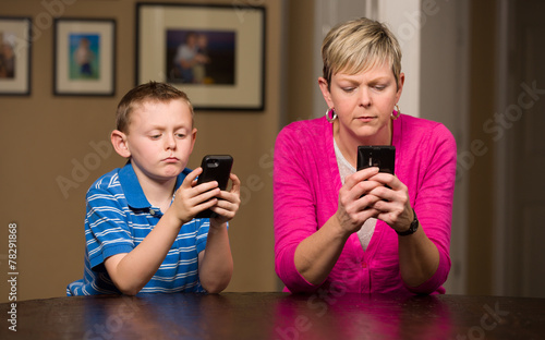 Mother and young son on mobile cell phones texting.