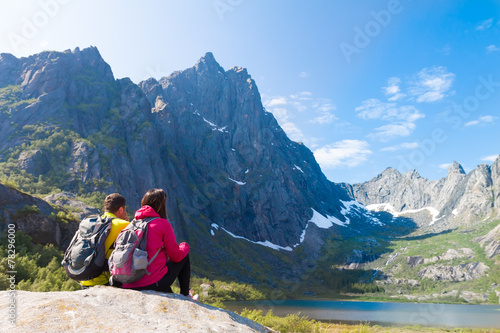 Young tourist couple sitting on stone near mountain lake