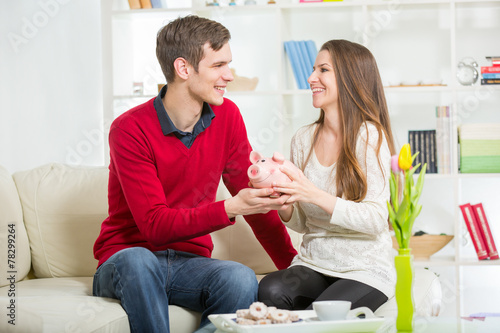 Young happy couple holding a piggy bank in the living room