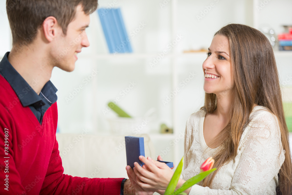 Boyfriend surprising his girlfriend with gift, in the living roo Boyfriend surprising his girlfriend with gift, in the living roo