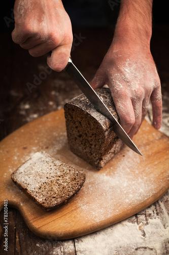 Male hands slicing fresh bread on table