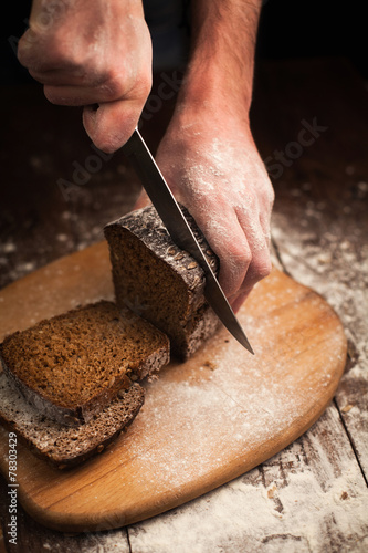 Male hands slicing fresh bread on table