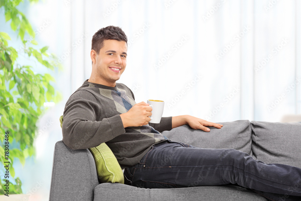 Man drinking coffee seated on sofa at home