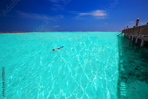 Young man snorkling in tropical lagoon with over water bungalows
