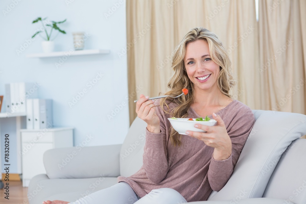 Smiling blonde sitting on couch eating salad Smiling blonde sitting on couch eating salad