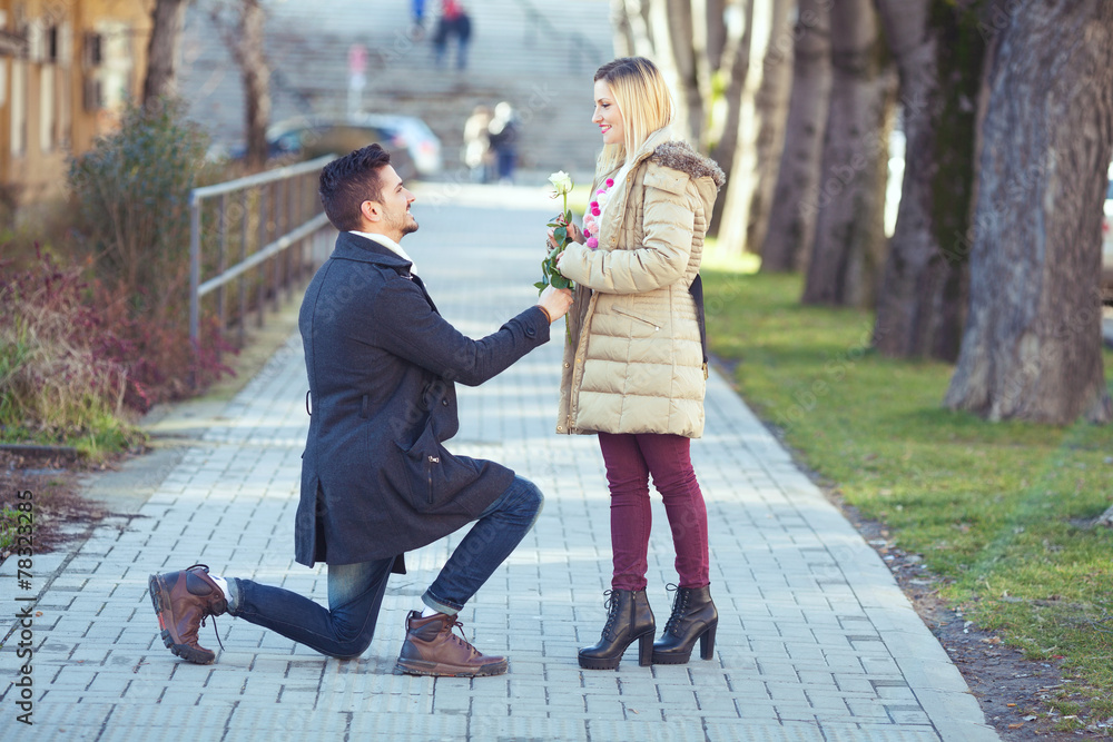 Obraz premium Romantic young man with a rose kneeling