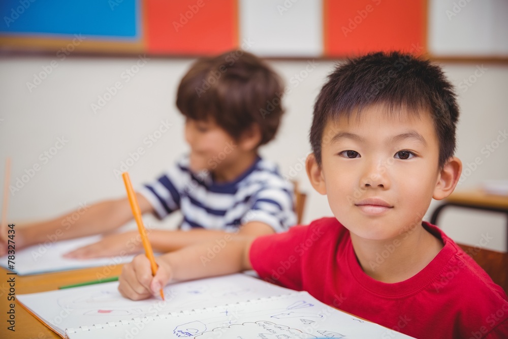 Cute pupils drawing at their desks one smiling at camera Cute pupils drawing at their desks one smiling at camera