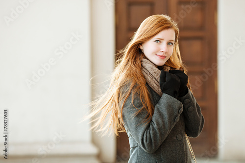 Young redhead woman wearing coat and scarf posing outdoors © sergeyzapotylok