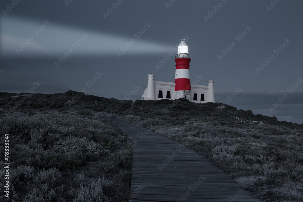 Lighthouse with shining light in darkness and dark blue clouds a