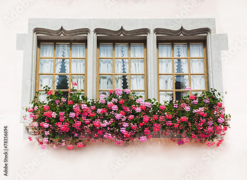Three windows in old house with pink flowers