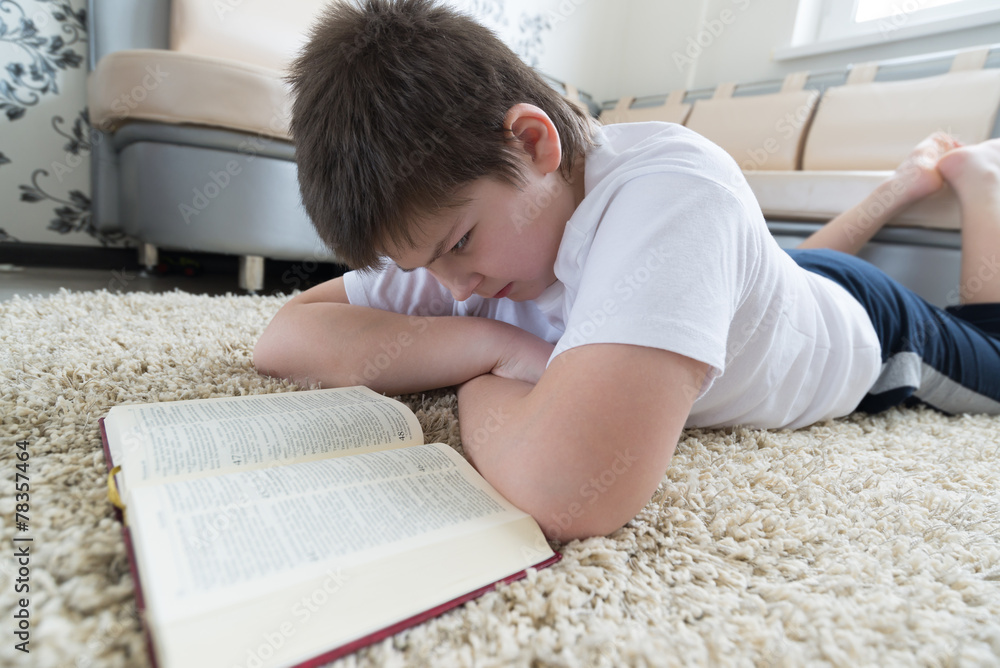 Boy reading a book while lying on carpet in the room Boy reading a book while lying on carpet in the room