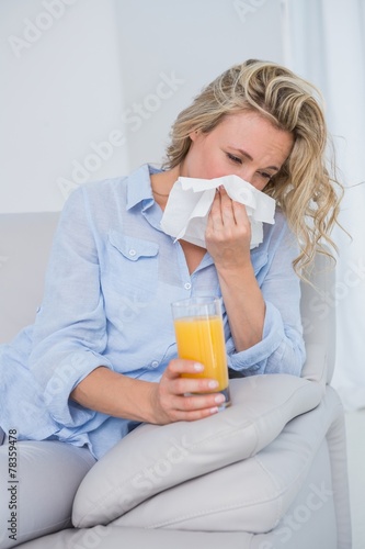 Blonde sneezing on tissue and holding glass of orange juice